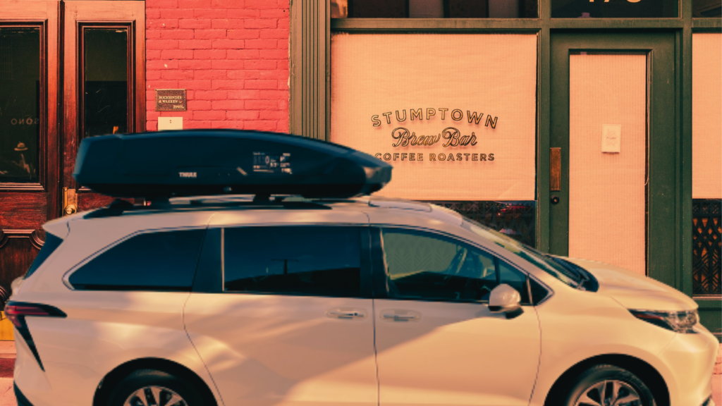 She parks her white Toyota Sienna on street with a black aerodynamic thule motion xt cargo box.