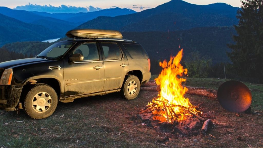 a thin car roof box on top of black Cadillac SUV beside a camping fire